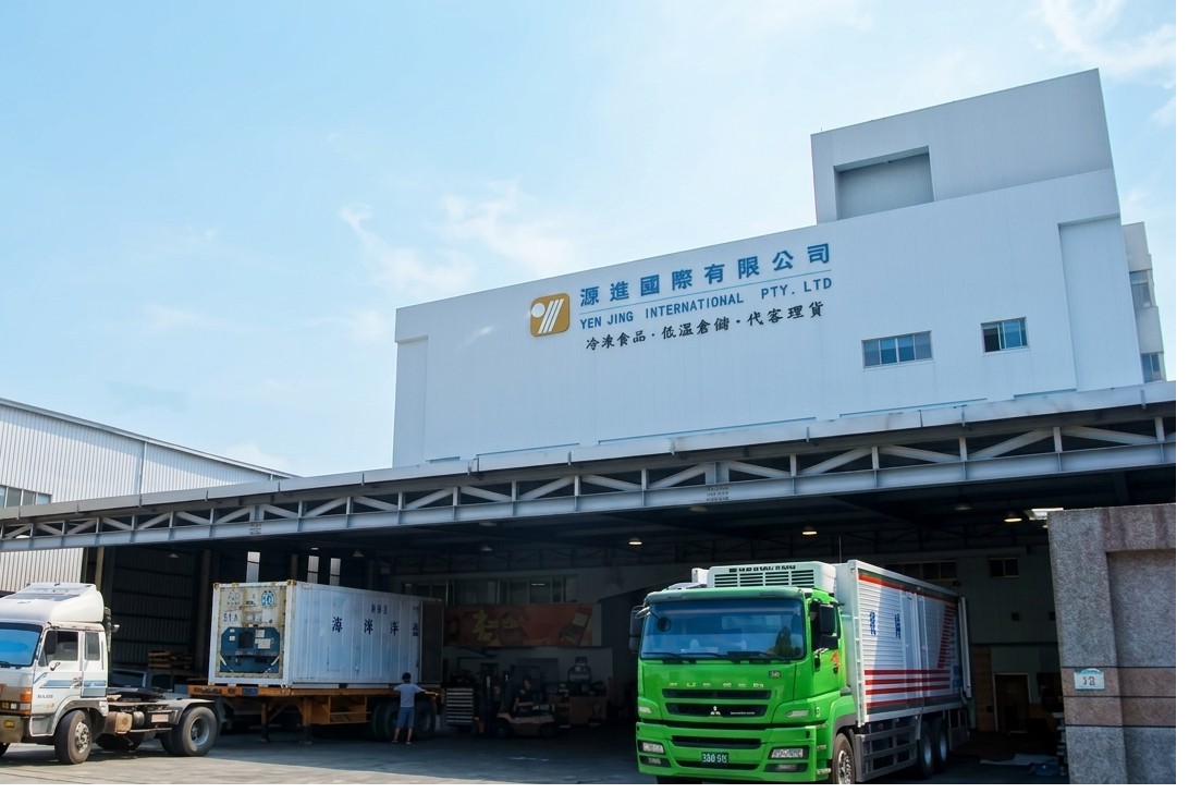 Exterior of the Kaohsiung Xiaogang cold storage facility — Yen Jing International signage above loading bays with refrigerated trucks and containers at the dock.