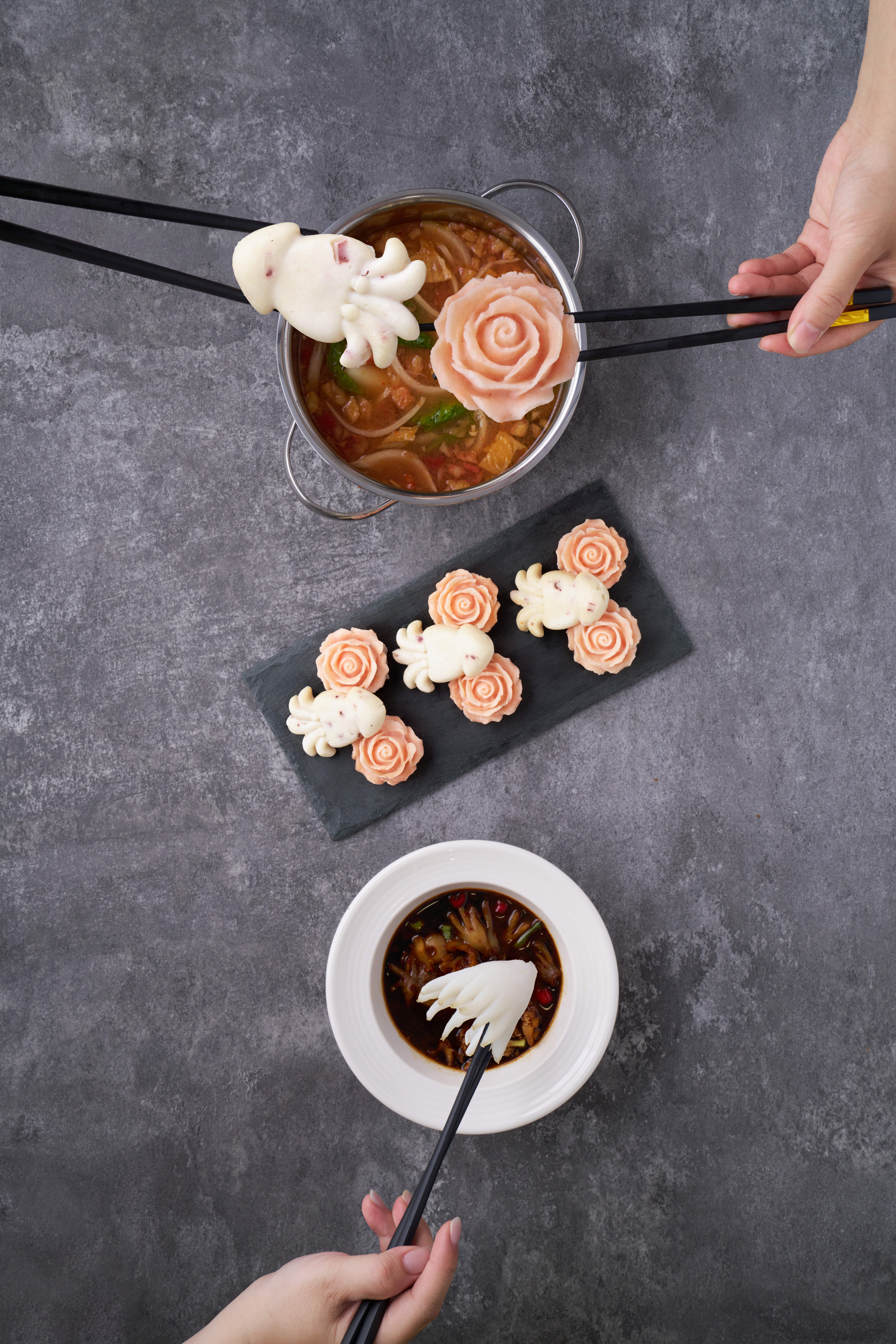 Surimi value-added showcase — overhead studio shot of rose-shaped surimi fishballs on a slate, alongside a tomato hotpot lifting an octopus and a rose-surimi piece, and a dipping bowl with shaped surimi at the bottom of frame.