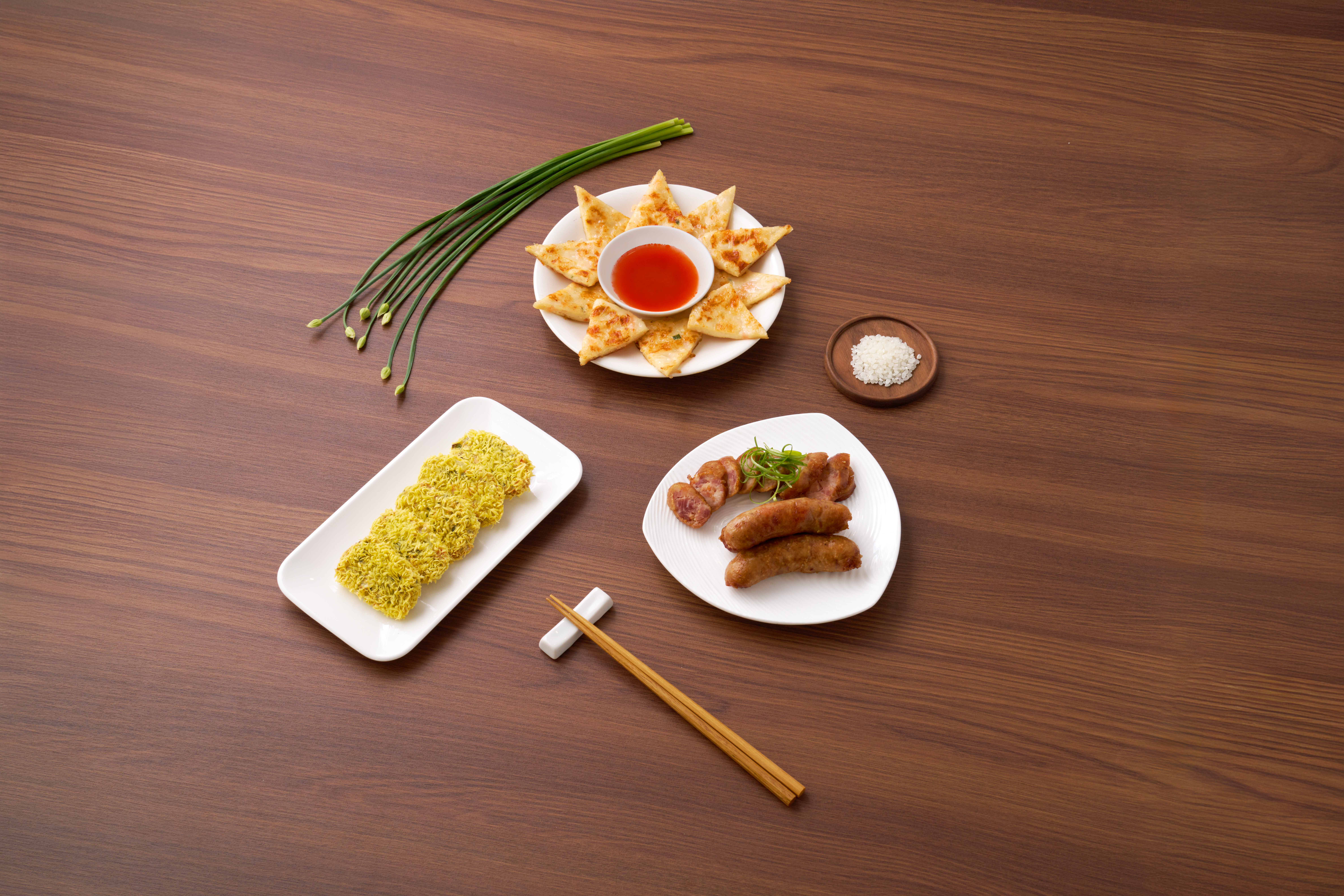 Value-added tier — overhead studio shot of formed and finished products: pan-fried squid cakes with chili dipping sauce, surimi-paste fishball nests on a rectangular dish, and grilled seafood sausages.